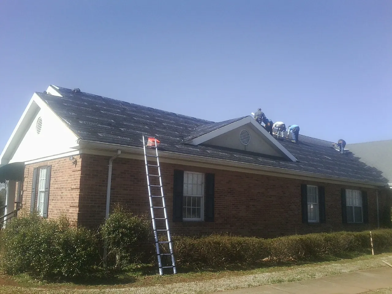 Crew tearing shingles off a brick ranch roof with a ladder set — Emergency Roof Repair work by our crew in Sikeston