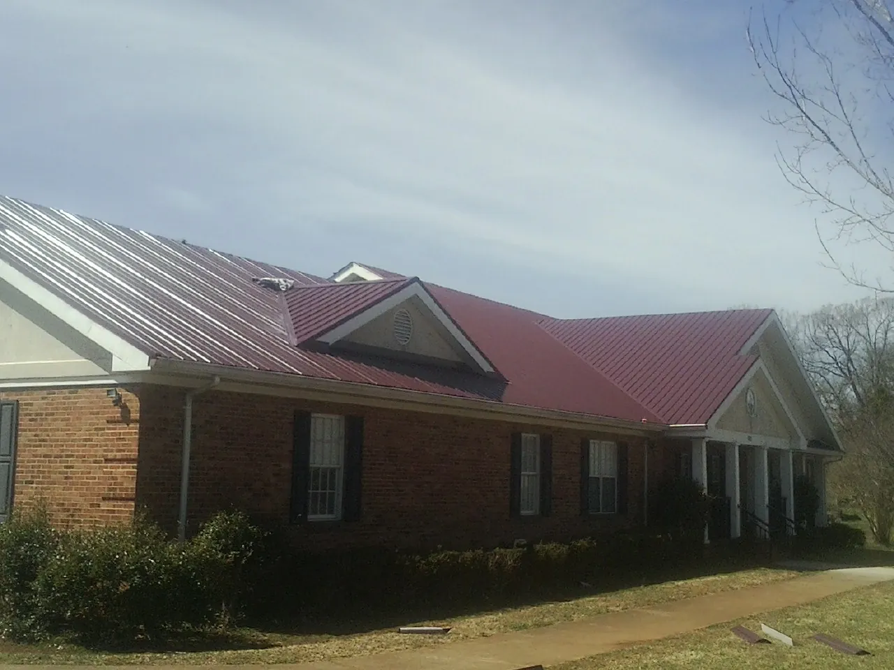 Red metal roof with gabled entries on a long brick building, from a Hail Damage Roof Repair job in Sikeston