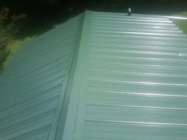 New green metal panels meeting at the ridge of a roof — Flat Roof Repair work by our crew in Sikeston