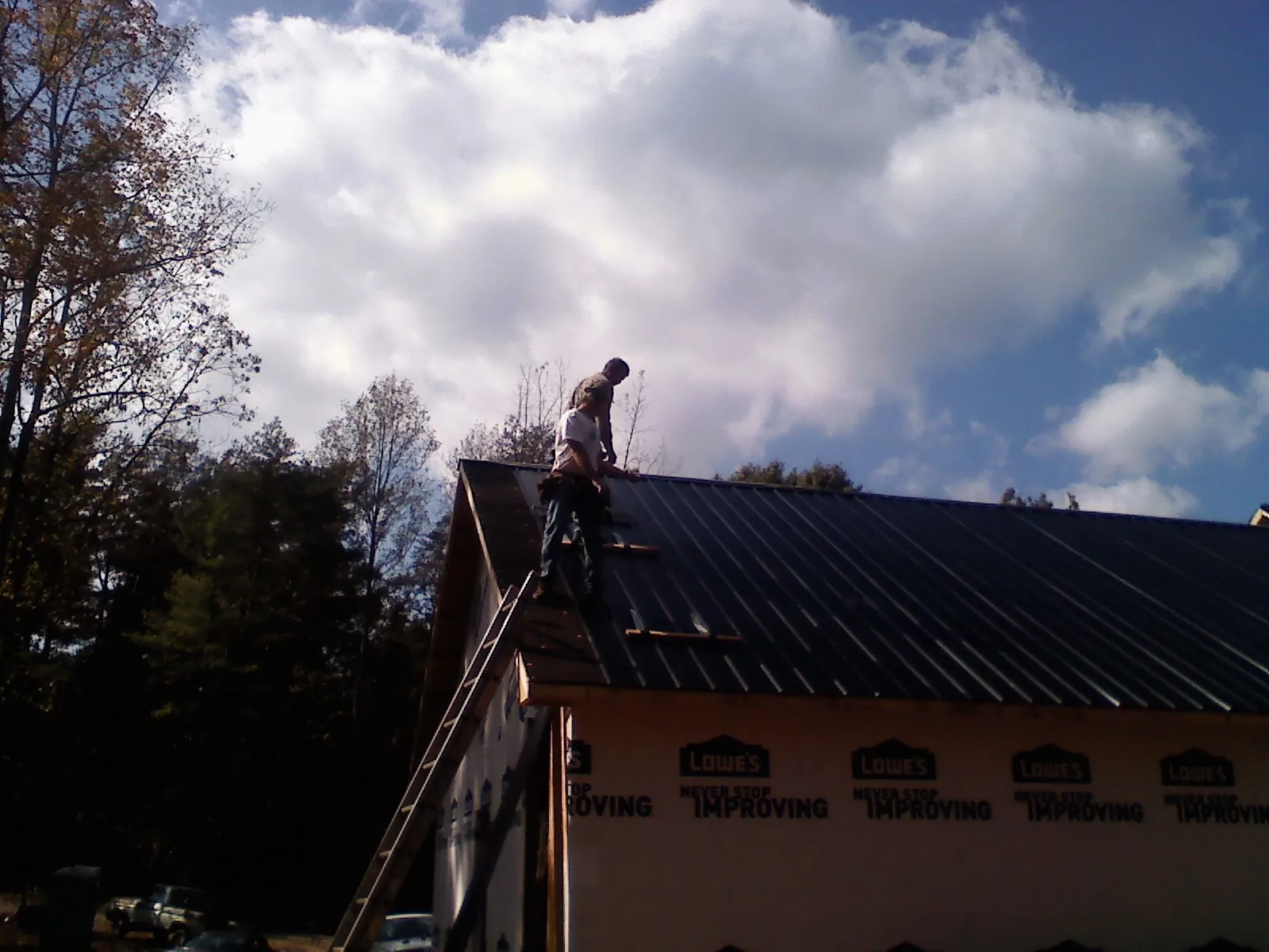 Roofer fastening dark metal panels high against a cloudy sky, from a Roof Inspection job in Sikeston
