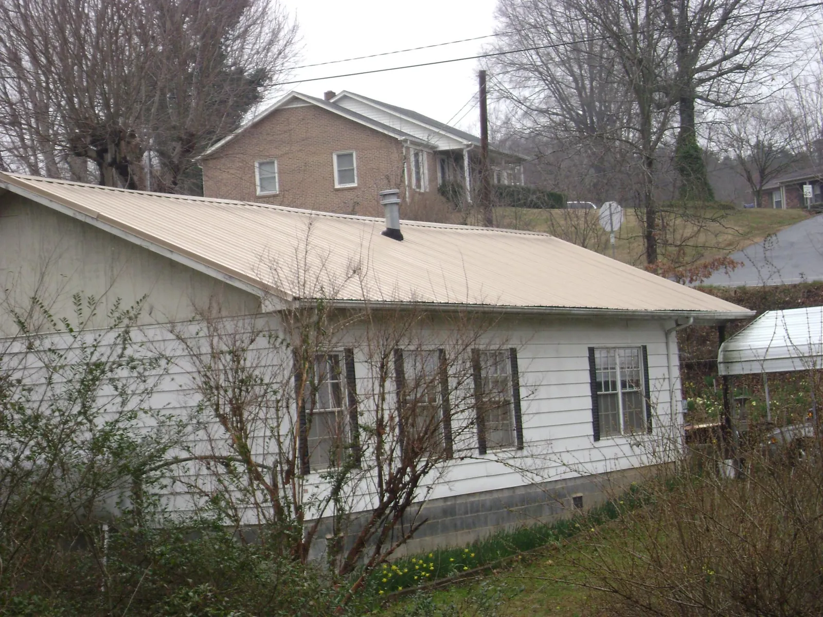 Tan metal roof on a white sided house set into a hillside — Commercial Roofing by Roofing Brothers in Sikeston