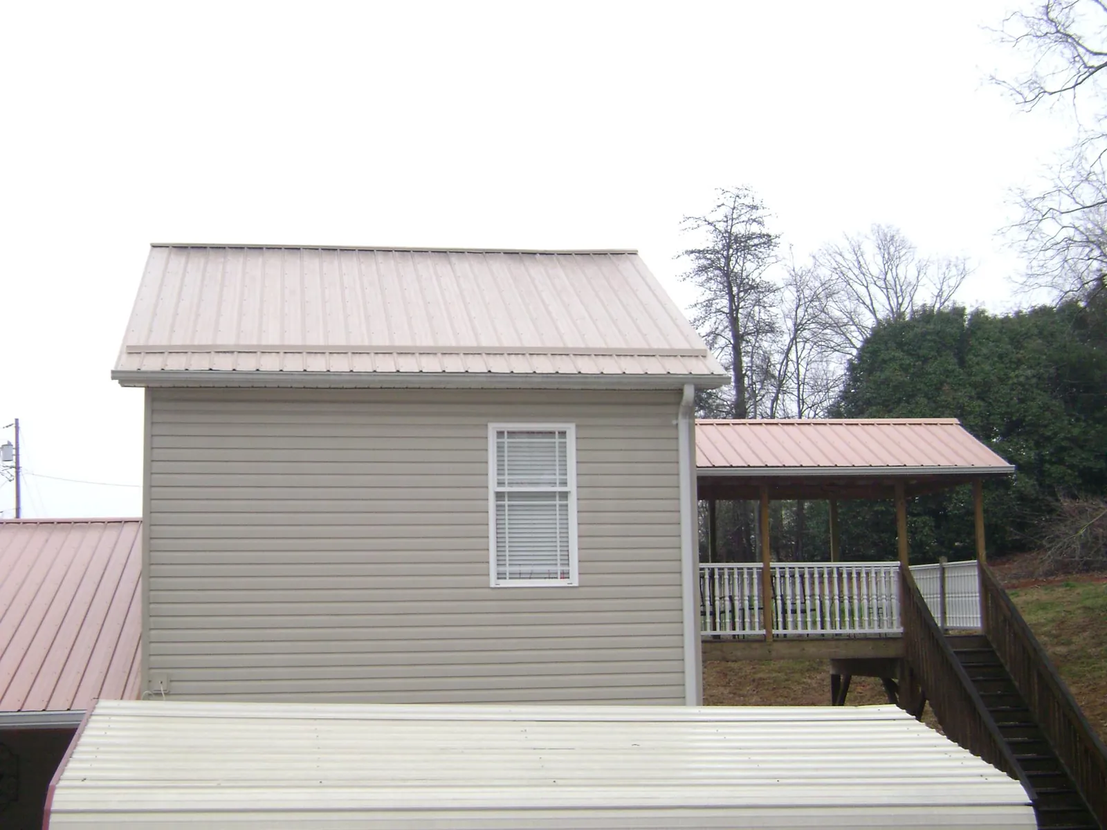 Tan metal roofs on a two story addition and attached porch, from a Roof Replacement job in Sikeston